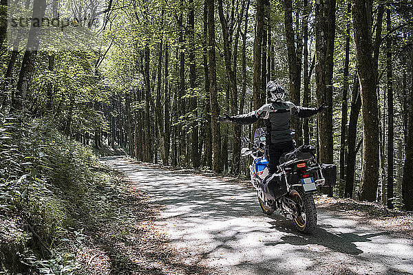 Motorradfahrer auf einer Fahrt auf einem Waldweg mit ausgestreckten Armen