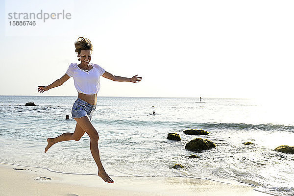 Schöne Frau rennt und springt vor Freude am Strand