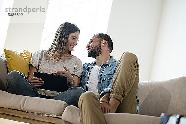 Glückliches junges Paar entspannt zu Hause auf der Couch mit Tablette