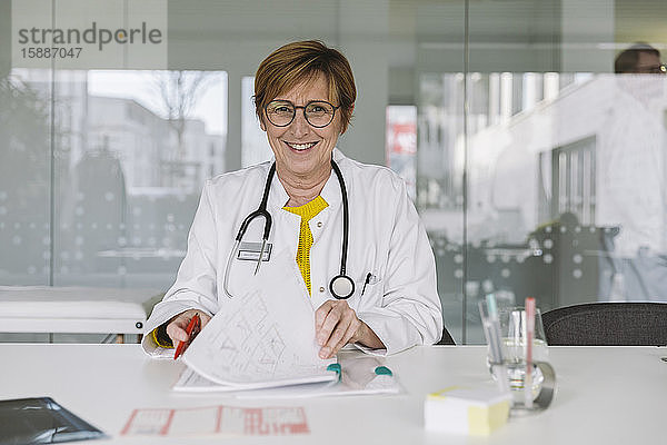 Porträt eines lächelnden Arztes am Schreibtisch sitzend