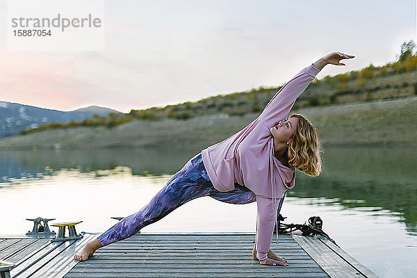 Junge Frau macht Yoga auf einem Steg  Dreieckshaltung