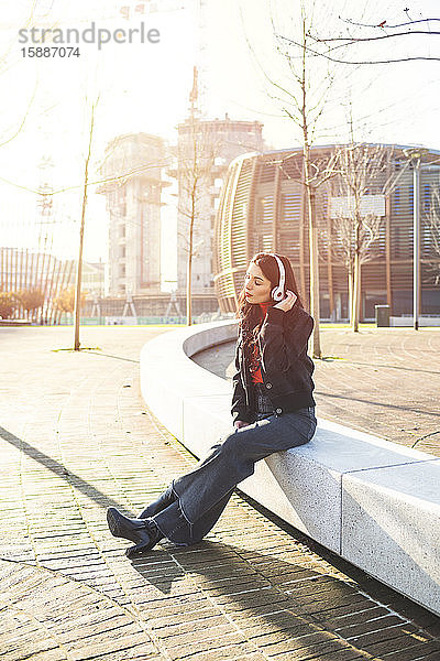 Schöne Frau sitzt auf einer Bank  benutzt ein Smartphone und hört Musik