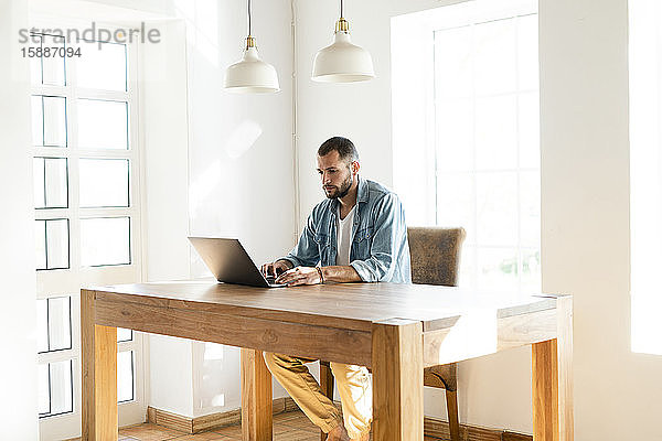 Junger Mann arbeitet zu Hause an seinem Laptop im Heimbüro im modernen Wohnzimmer