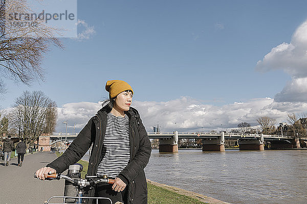 Frau mit Fahrrad am Flussufer  Frankfurt  Deutschland