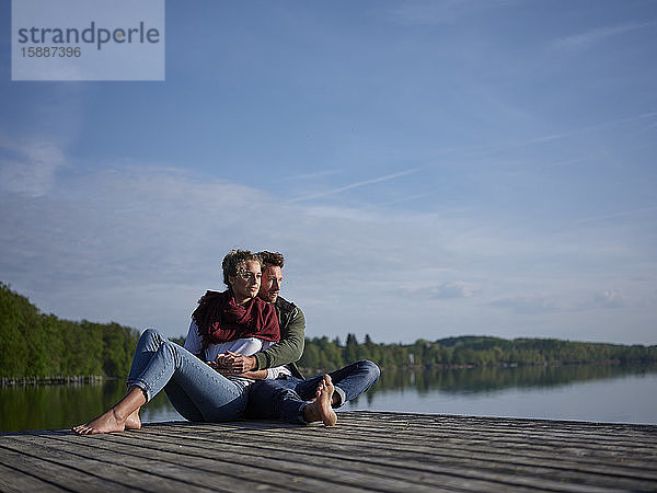 Romantisches Paar sitzt auf einem Steg am See