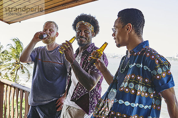 Männliche Freunde unterhalten sich beim Biertrinken auf dem Balkon