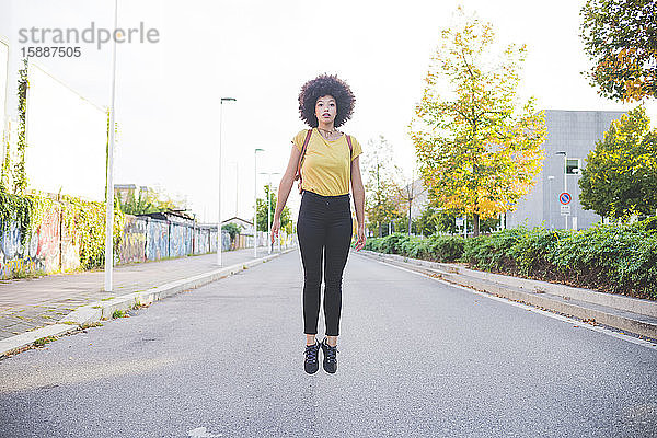 Junge Frau mit Afro-Frisur springt auf eine Straße in der Stadt