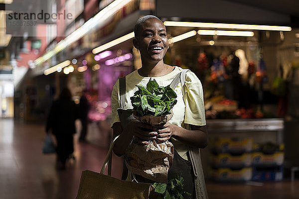 Porträt einer glücklichen Frau mit Papiertüte in der Hand in einer Markthalle