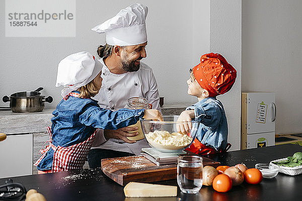 Vater mit zwei Kindern bereitet zu Hause in der Küche Teig für selbstgemachte glutenfreie Nudeln zu