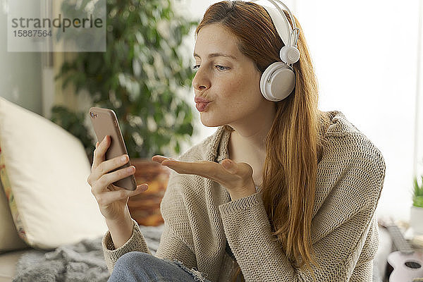 Junge Frau mit Kopfhörern und Smartphone beim Chatten zu Hause