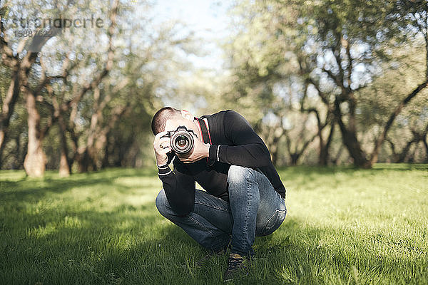 Mann kauert auf einer Wiese und fotografiert mit der Kamera