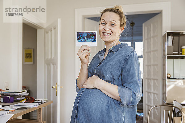 Porträt einer glücklichen Schwangeren  die zu Hause ein Ultraschallbild zeigt