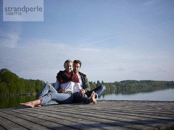 Romantisches Paar sitzt auf einem Steg am See