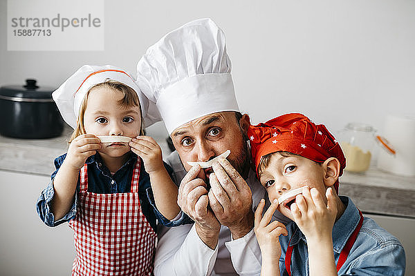 Verspielter Vater mit zwei Kindern  der sich beim Zubereiten von hausgemachter Pasta in der heimischen Küche amüsiert