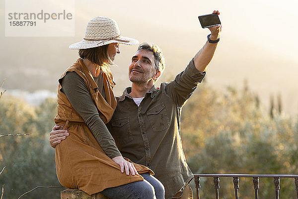 Paar beim Selbstfahren mit dem Smartphone während des Sonnenuntergangs auf dem Land
