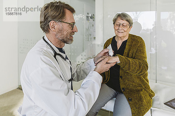Arzt legt Salbe auf die Hand eines älteren Patienten