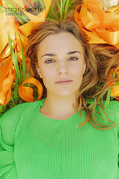 Bildnis einer in einem Feld mit orangefarbenen Bändern liegenden jungen Frau