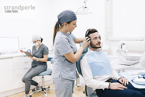 Medizinische Sekretärin bereitet Zahnbehandlung vor  setzt Kopfhörer auf den Kopf des Patienten auf