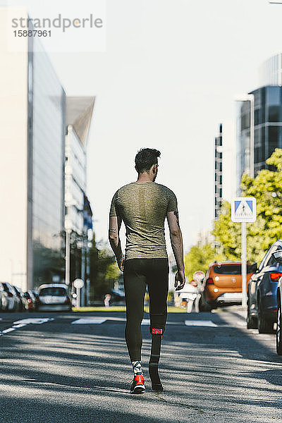 Rückansicht eines behinderten Sportlers mit Beinprothese beim Gehen auf einer Straße in der Stadt