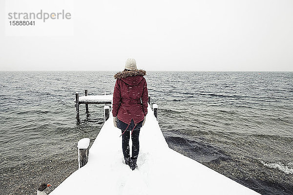Rückenansicht einer jungen Frau  die auf einem schneebedeckten Steg am Starnberger See steht  Deutschland