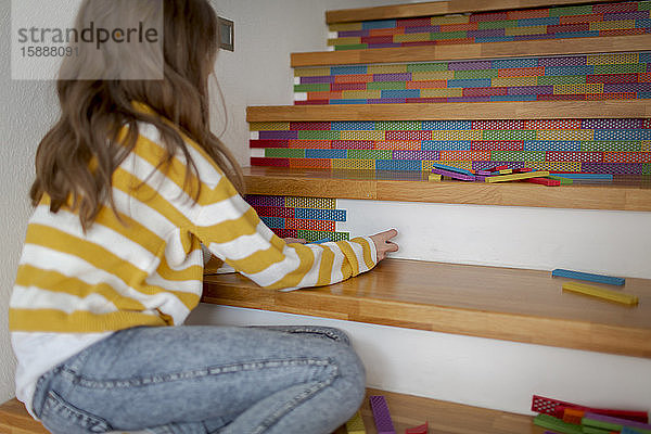 Rückansicht eines Mädchens  das auf einer Treppe sitzt und mit Holzklötzen spielt