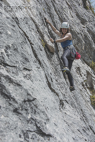 Weibliche Bergsteigerin klettert an Felswand
