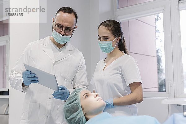 Junge Frau erhält Zahnbehandlung in Klinik  Denist und Assistentin mit digitalem Tablett