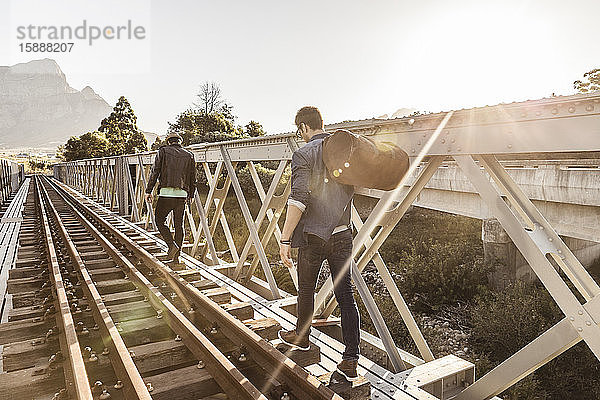 Rückansicht von zwei Männern  die auf einer alten Eisenbahnbrücke gehen