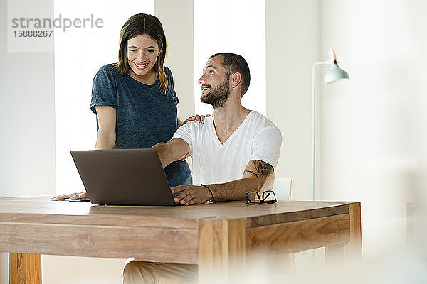 Lächelndes Paar bei der Arbeit am Laptop von zu Hause im Home-Office im modernen Wohnzimmer