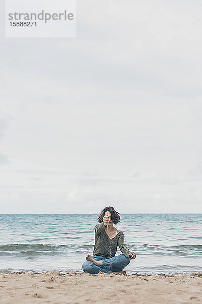 Junge Frau sitzt am Strand  Sand rieselt durch ihre Hände