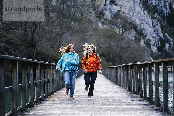 Zwei glückliche Frauen laufen zusammen auf der Strandpromenade  Valdemurio-Stausee  Asturien  Spanien