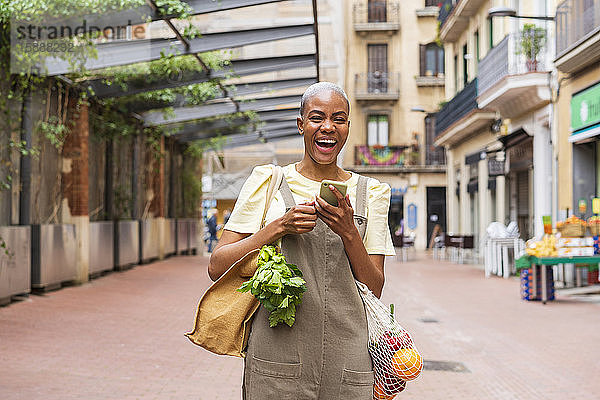 Lachender Mann mit Einkaufstüte und Handy in der Stadt