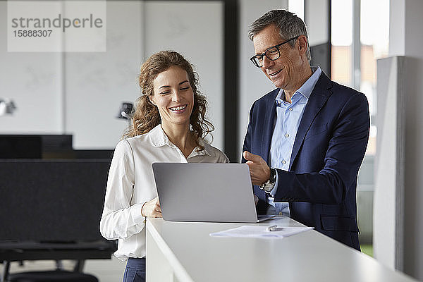 Lächelnder Geschäftsmann und Geschäftsfrau arbeiten gemeinsam am Laptop im Büro