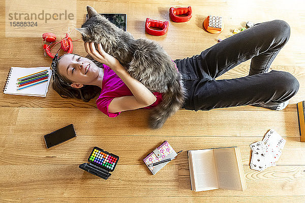 Auf dem Boden liegendes Mädchen  kuschelnde Katze  umgeben von Spielgeräten