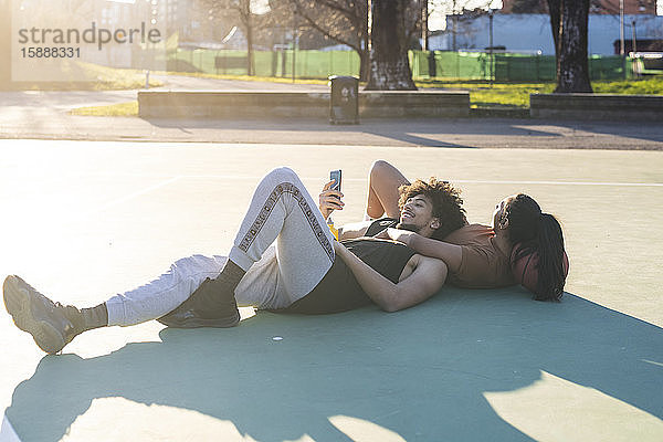 Sportliches junges Paar macht Pause auf Basketballfeld liegend