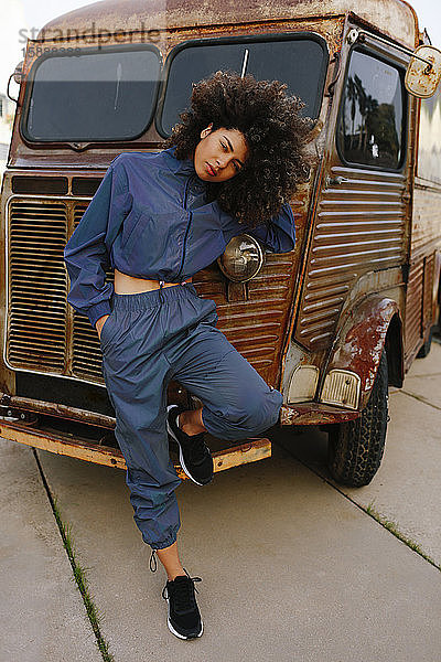 Porträt einer eleganten jungen Frau im Trainingsanzug  die sich an einen alten Lieferwagen lehnt