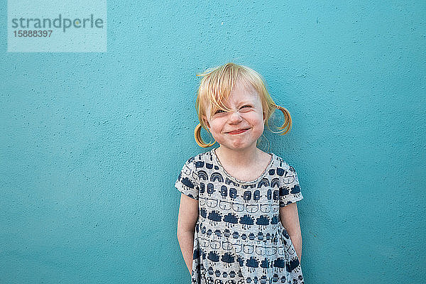 Porträt eines grinsenden kleinen Mädchens vor blauer Wand