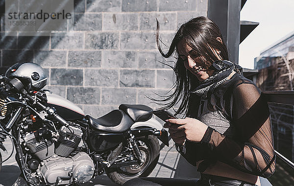 Junge Frau  die ein Smartphone neben ihrem Motorrad benutzt
