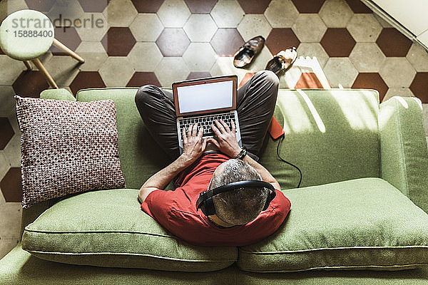 Reifer Mann sitzt auf dem Sofa und benutzt den Laptop  hört Musik