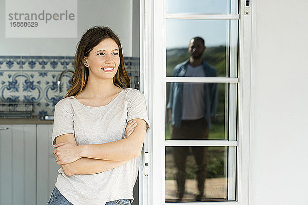 Lächelnde junge Frau lehnt an der Tür und sieht ihren Freund an  der draußen steht