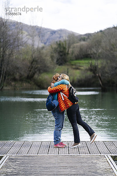 Zwei glückliche Frauen mit Rucksäcken stehen auf einem Steg und umarmen sich  Stausee Valdemurio  Asturien  Spanien