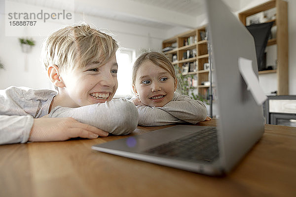 Glückliche Geschwister schauen zu Hause gemeinsam auf den Laptop