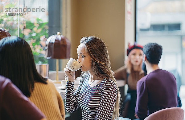 Junge Frau sitzt in einer belebten Bar eines Restaurants und trinkt Kaffee