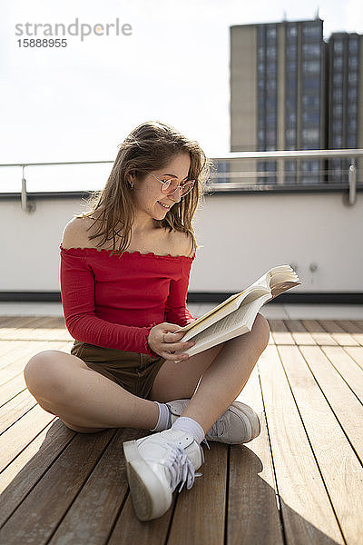 Lächelnde junge Frau liest ein Buch auf dem Dach