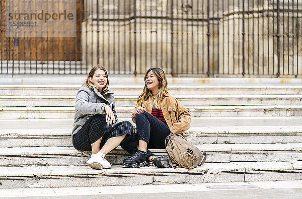 Zwei glückliche junge Frauen sitzen auf einer Treppe in der Stadt