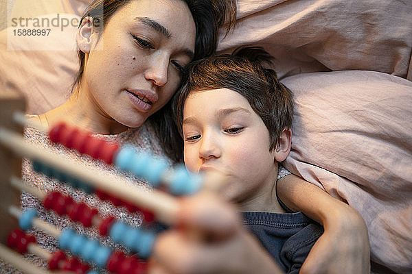 Mutter und kleiner Sohn liegen zusammen auf dem Bett und benutzen einen Abakus