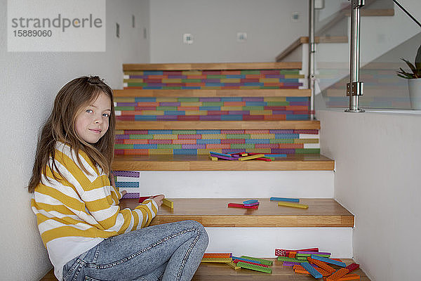 Porträt eines Mädchens  das auf einer Treppe sitzt und mit Holzklötzen spielt