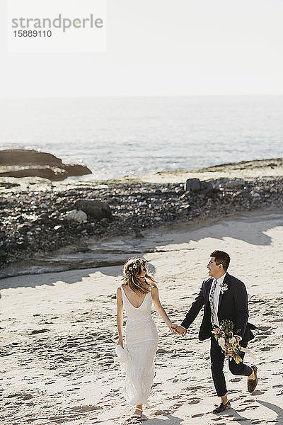 Glückliches Brautpaar beim Spaziergang am Strand