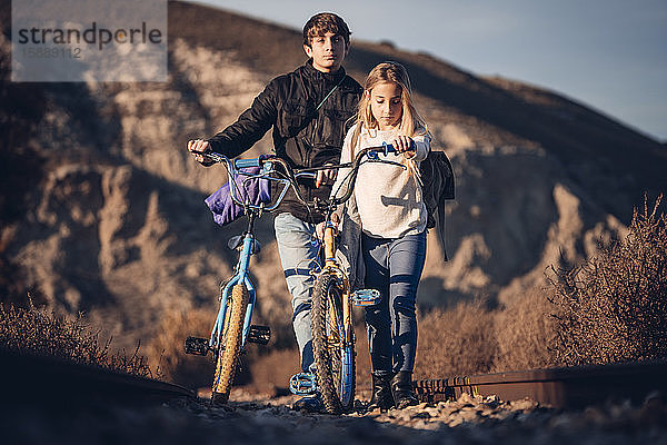 Junge und Mädchen zu Fuß mit Fahrrädern in ländlicher Landschaft