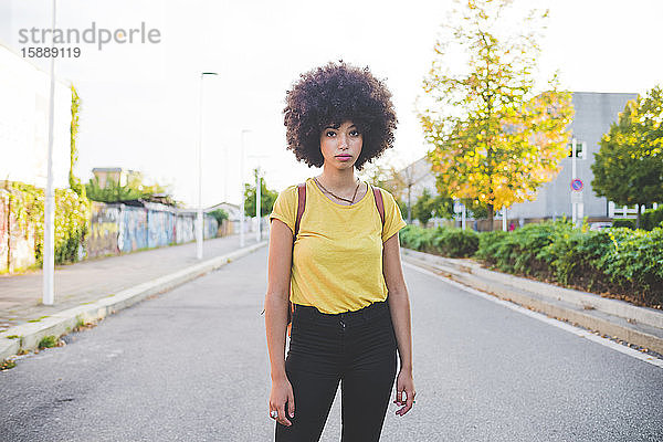 Porträt einer jungen Frau mit Afrofrisur  die auf einer Straße in der Stadt steht